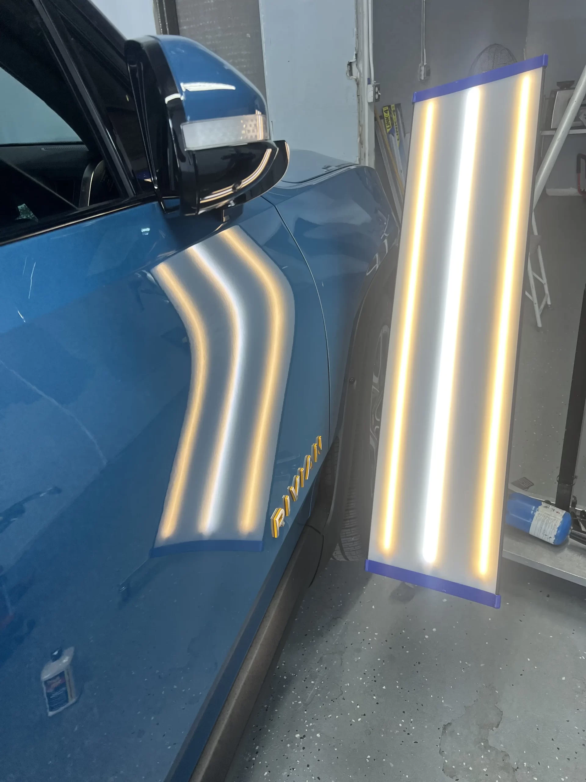The right side of a blue Rivian is being lit up for inspection after repairs.