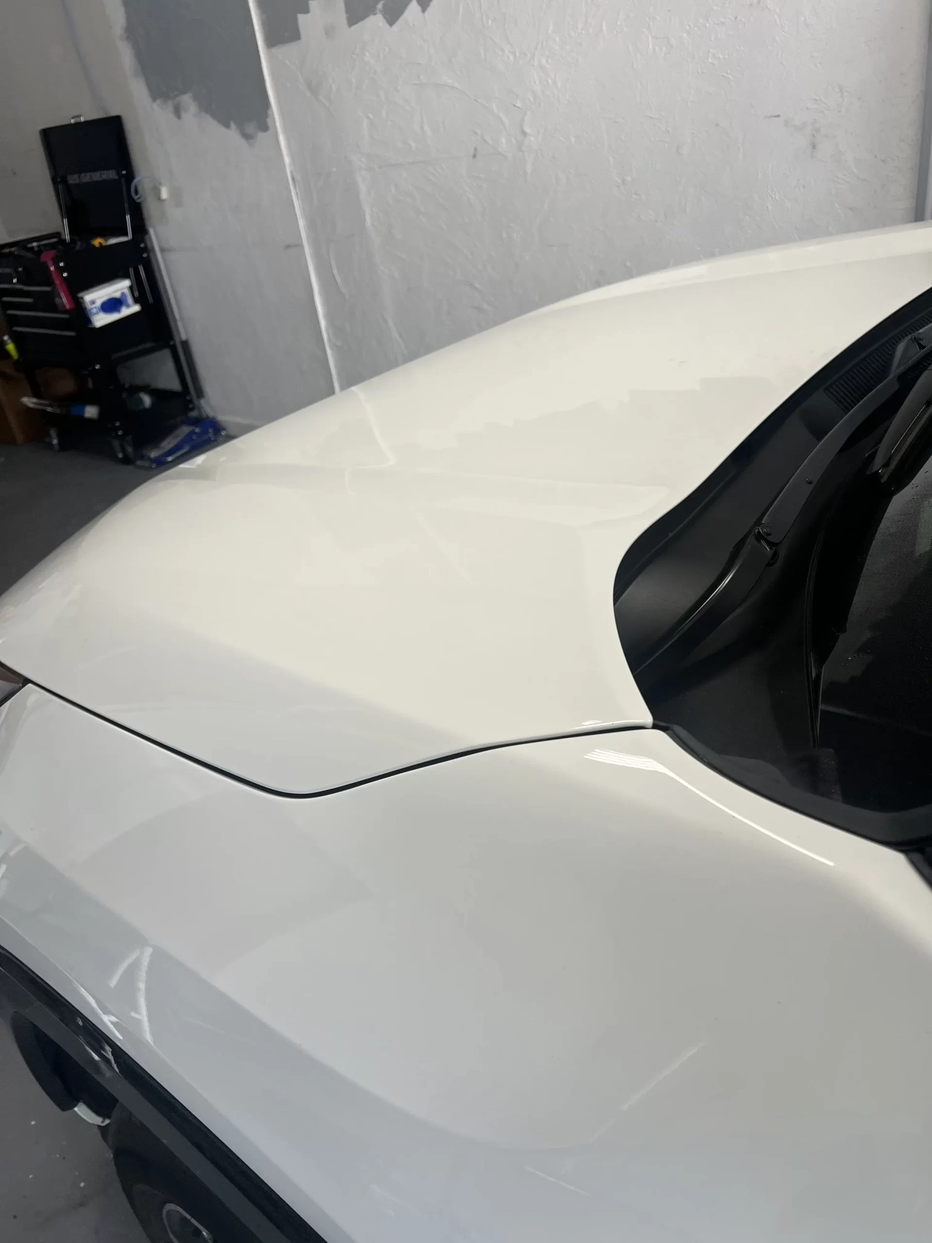 The repaired hood of a white vehicle inside a white-walled garage.