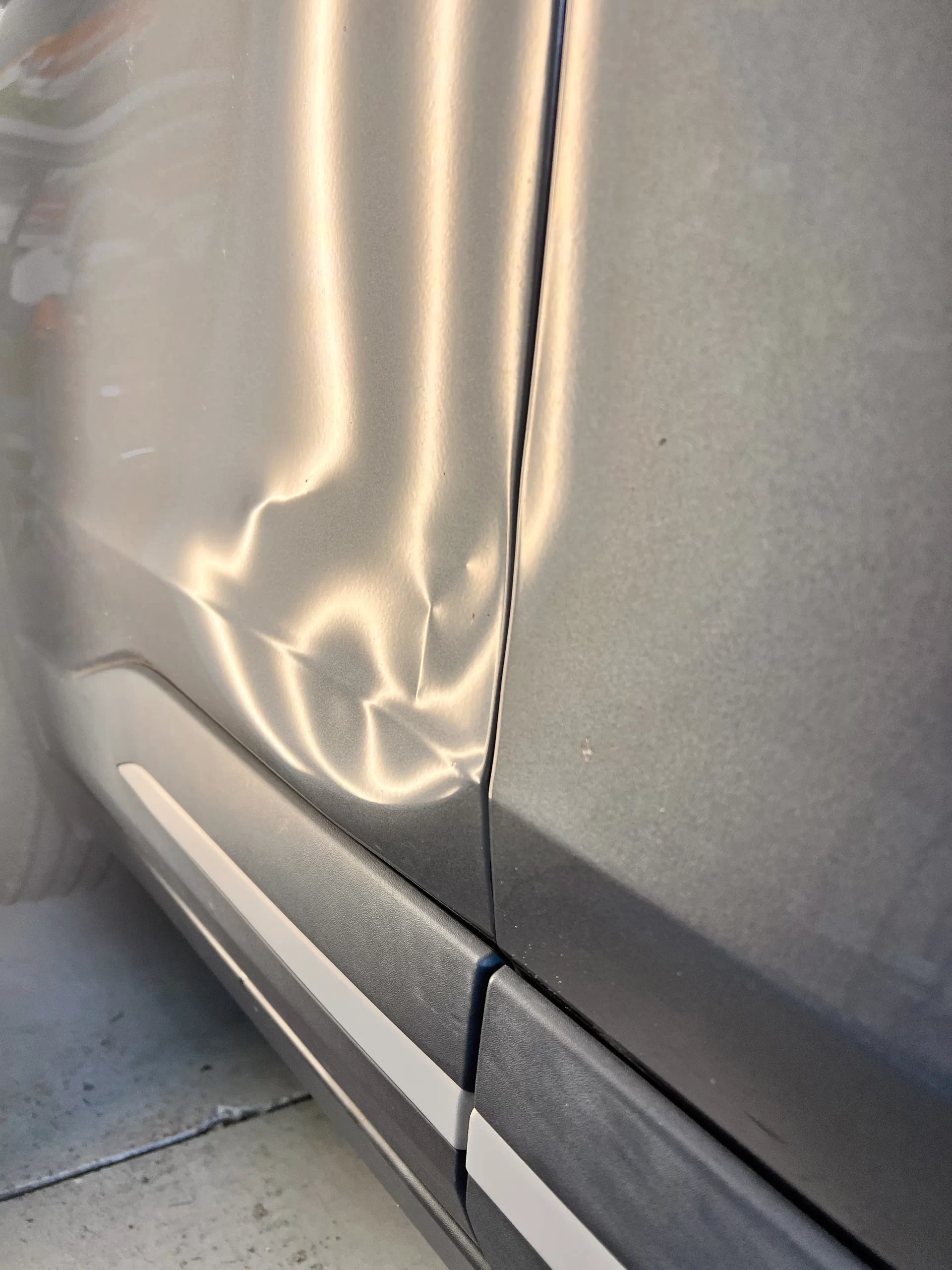 The slightly dented side of a grey vehicle before repairs.