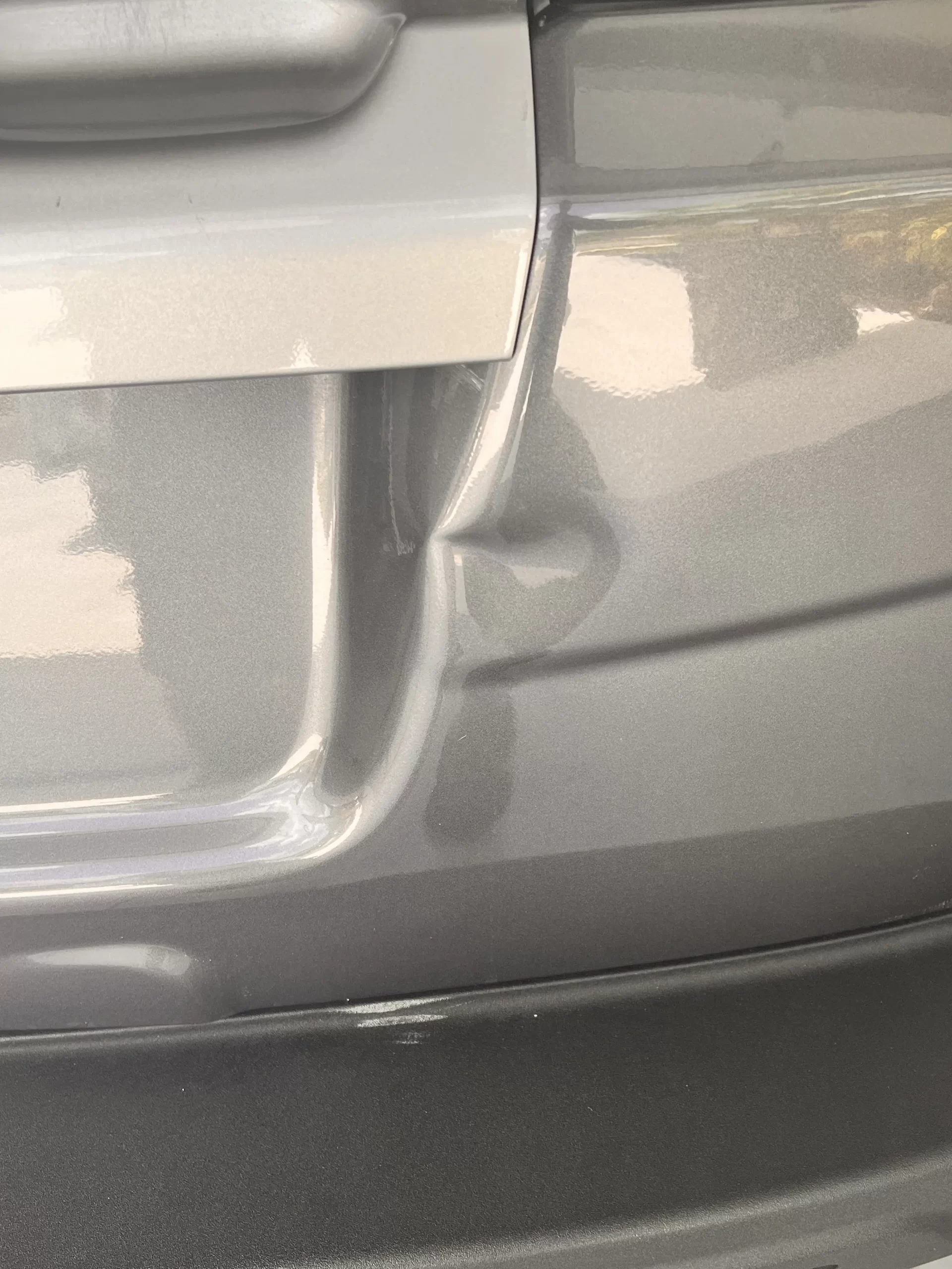 The slightly dented back portion of a grey vehicle prior to repairs.