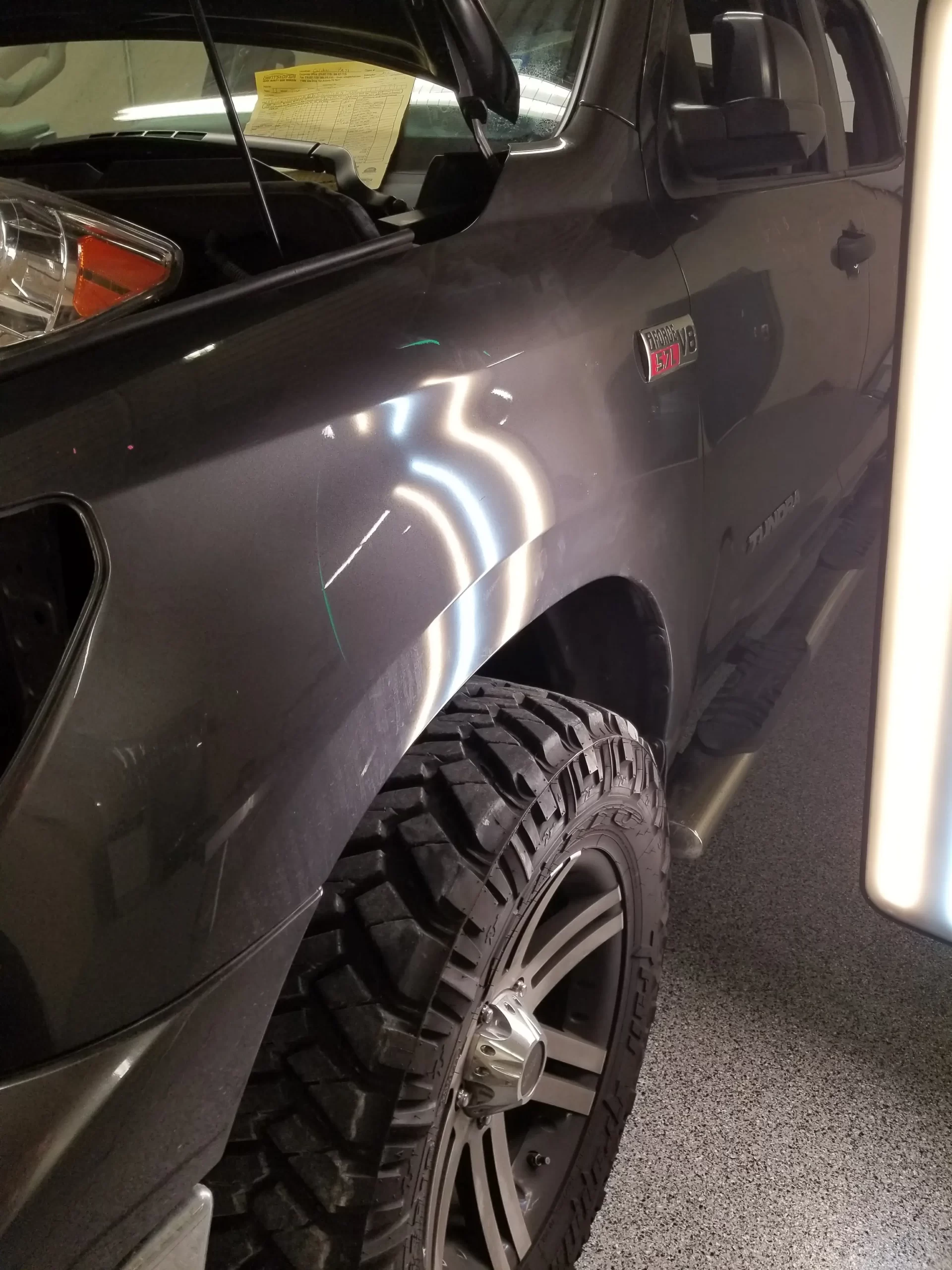 The side of a grey pickup truck is lit up after repairs.