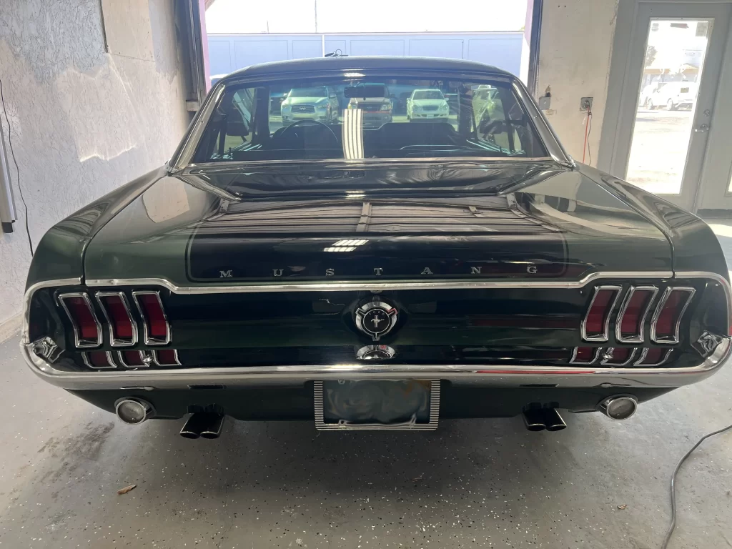 The rear end of a green Mustang in an auto garage.