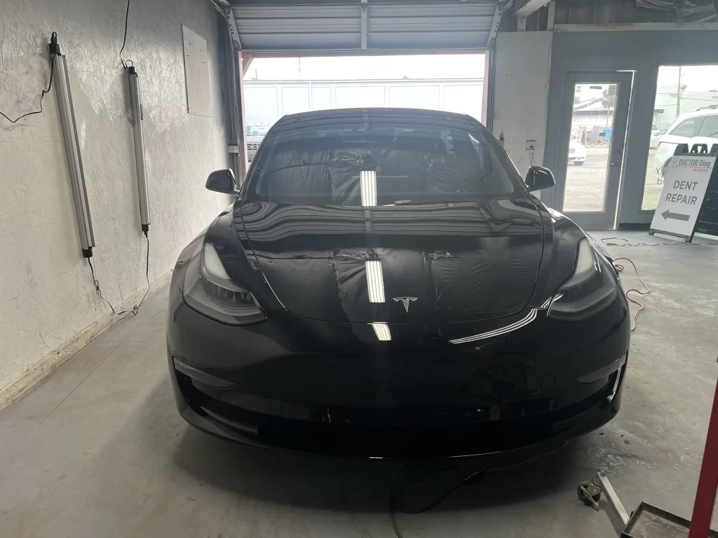 The front of a black Tesla is inside a car garage.